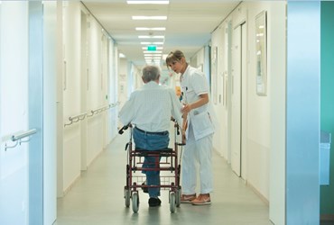 Verpleegkundige ondersteunt oude man met rollater