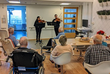 Op deze foto zie je een groep patiënten die luisteren naar muziek van violisten Andrea Torres en Egor Farafontov.