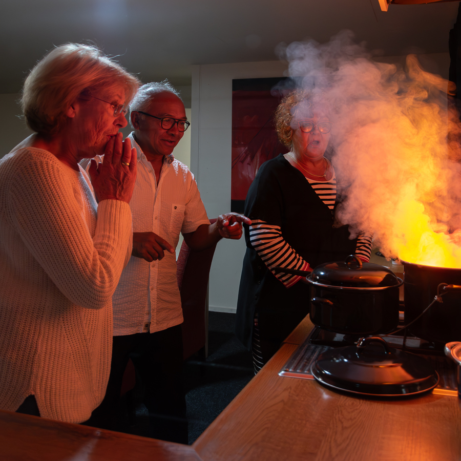 Juist handelen bij plotselinge brand in de keuken. Vrouw en man met een schrikreactie op vlam in de pan.