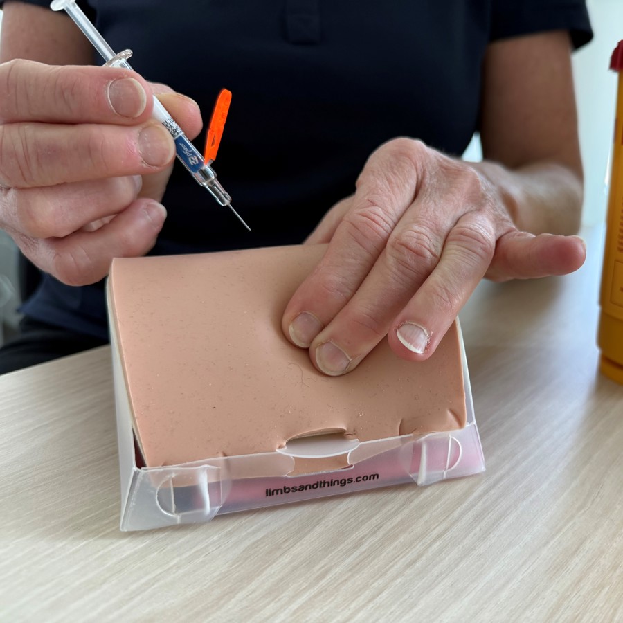 Op een oefenkussen leert de patiënt zelf een spuitje te zetten