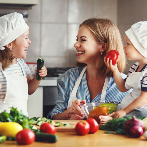 2 kinderen met koksmuts en kookschort en in het midden een vrouw met een kookschort