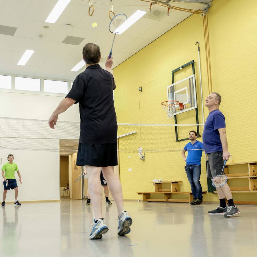 4 personen zijn binnen in een sportzaal aan het badmintonnen