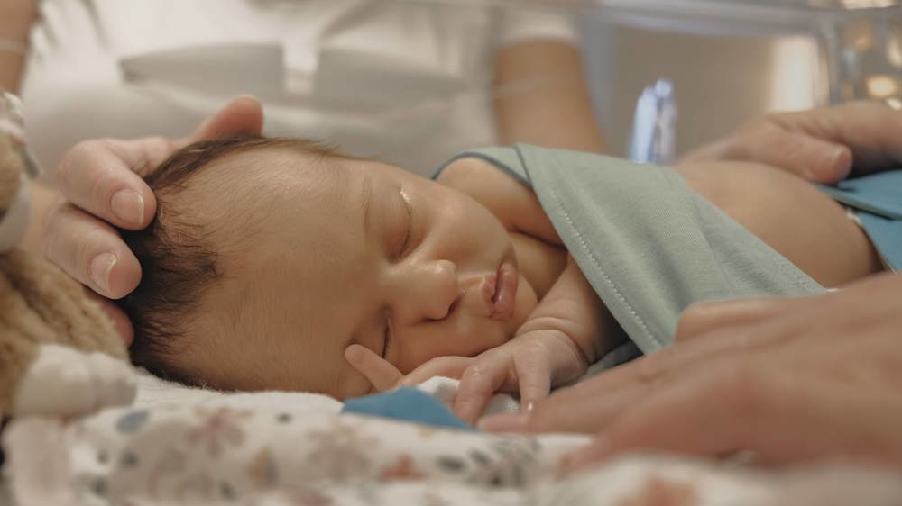 Baby in couveuse op afdeling Neonatologie/ Couveusesuite, moeders hand op hoofdje