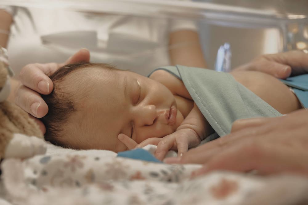 Baby in couveuse op afdeling Neonatologie/ Couveusesuite, moeders hand op hoofdje